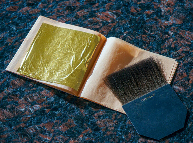 A thin sheet of gold leaf resting on a book beside a brush.