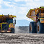 Two enormous autonomous Cat trucks haul ore at a mine.