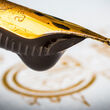 A golden nib holding a large drop of black ink.