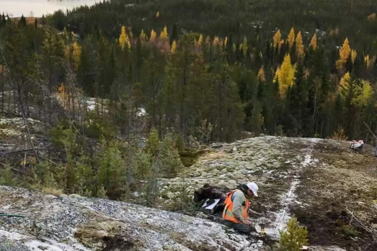 Geologist in hardhat, safety vest collecting samples from a channel cut in rock.