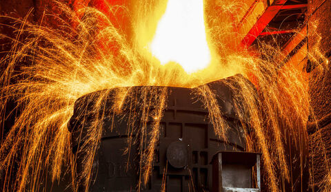 Sparks arc out of a vat being filled with molten steel.
