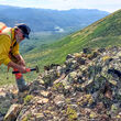 USGS geologist samples a mineralized outcrop on treeless slope in Alaska.