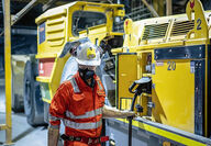A miner in safety gear plugs an electric underground loader into a charger.