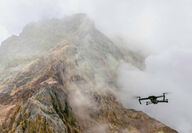 A drone flies by a mountain shrouded in clouds.