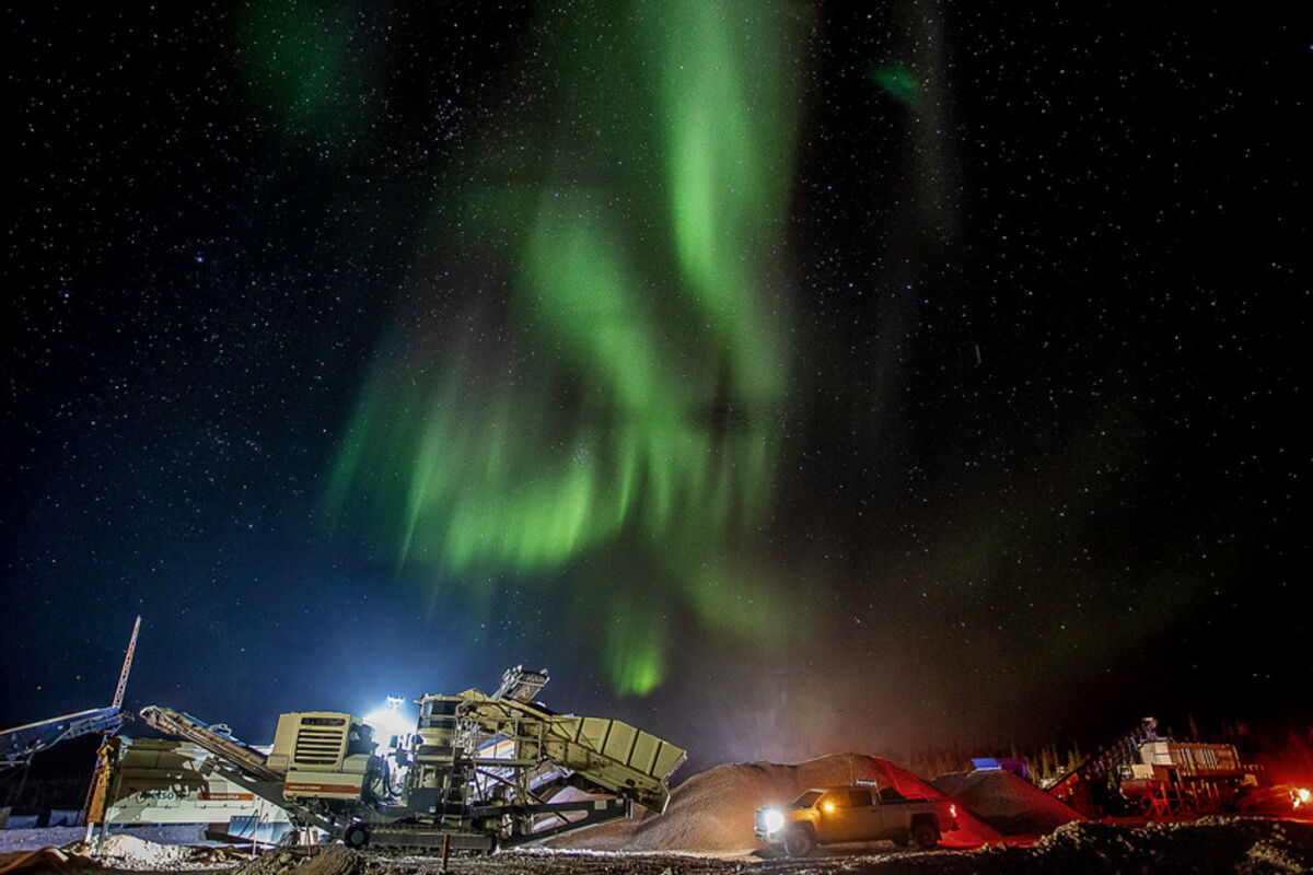 Vivid green northern lights display over mining equipment operating at night.