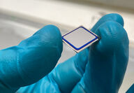 Blue-gloved hand holding a solar cell prototype.