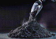 A scoop pours black graphene onto a pile.