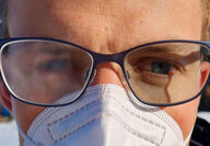 Closeup of person with mask and eyeglasses with one fogged and one clear lens.