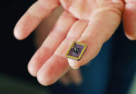 Closeup of epitaxial graphene electronics chip balanced on woman’s fingertip.