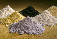 Six piles of white, yellow, grey, and black rare earth oxide powders.