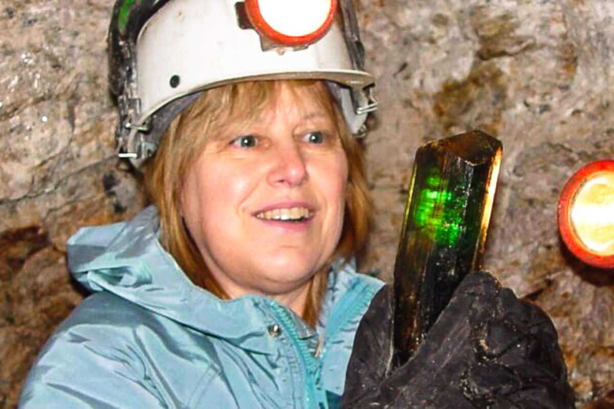 Mary Freeman holding a green tourmaline crystal in an underground cavern.