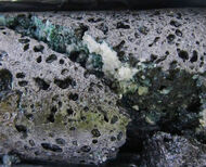 Drill core showing carbonate crystals along a fracture in hard grey basalt.