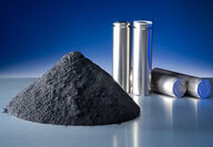 Pile of dark grey graphite anode powder next to four unlabeled silver batteries.