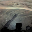 Flat Martian landscape with dunes, small rocks, and Perseverance’s shadow.