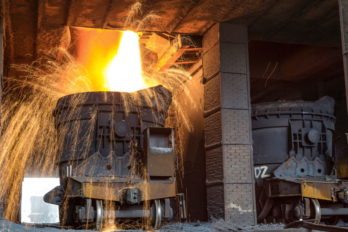 A shower of sparks arcs from molten steel being poured into an industrial vat.