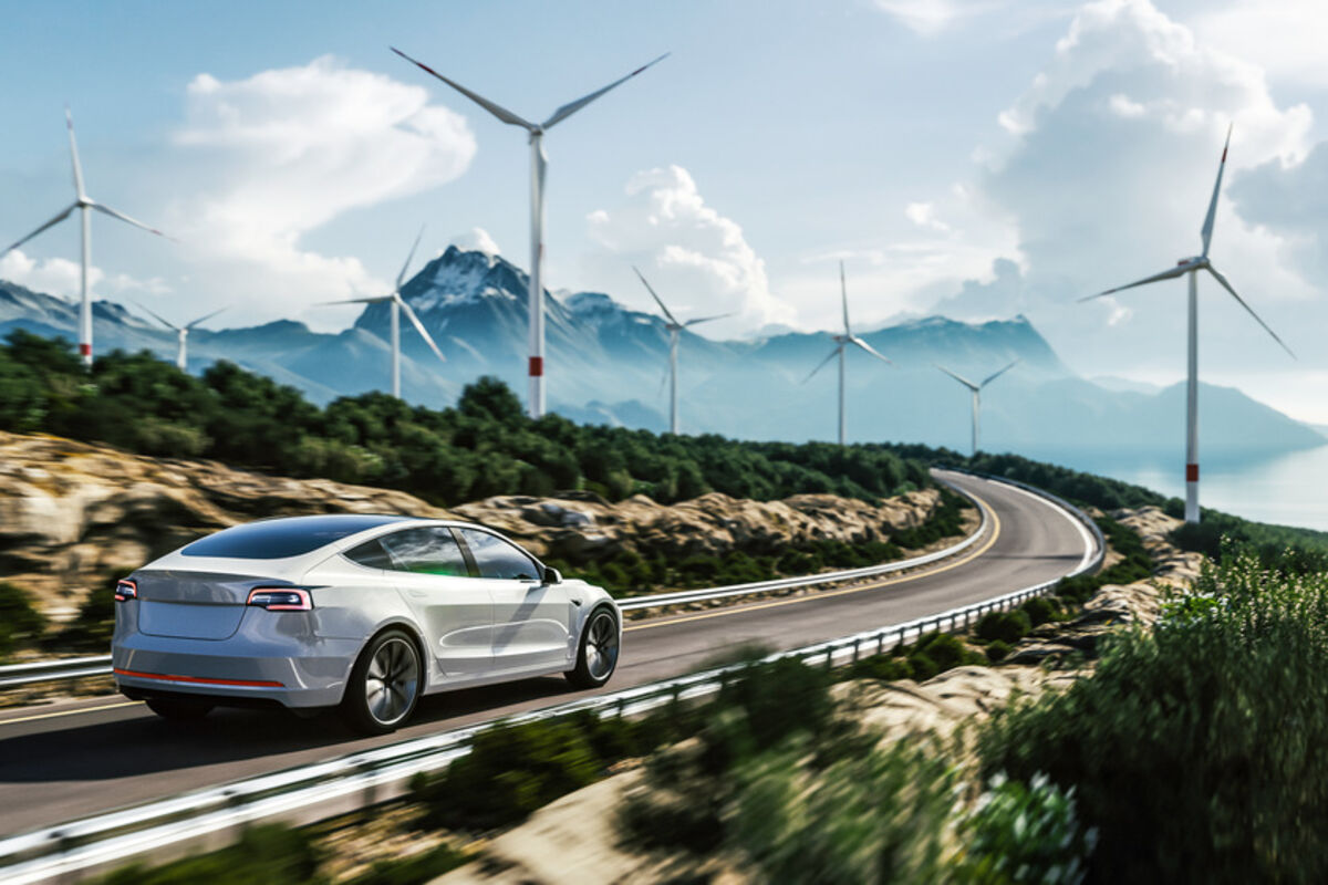 An EV drives past wind turbines on a rural road to the mountains.