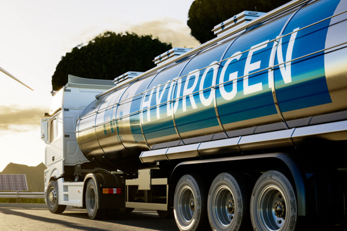 A semi-truck pulls a tanker marked hydrogen with wind turbine in the background.