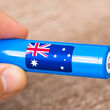 A hand holds a lithium battery cell with an Australia flag emblem on its side.