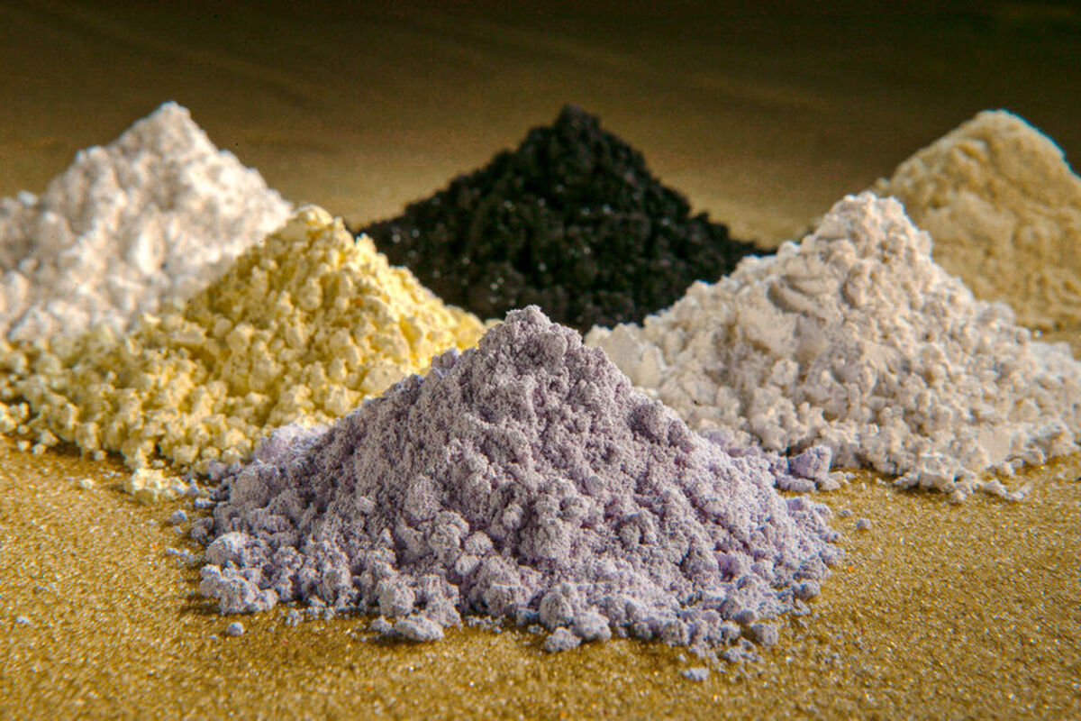 Piles of grey, yellow, black, and white rare earth oxide powders.