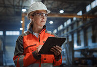 Female industrial worker with hard hat, safety equipment, and electronic tablet.