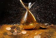A broken hourglass surrounded by pennies and glittering dirt