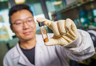 Scientist Lui Ping holds glass vial of lithium-sulfur cathode powder.