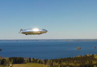 A silver hydrogen airship flies over a lake during the summer in Finland.