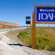 A blue “Welcome to Idaho” sign along a desert highway at the Nevada border.