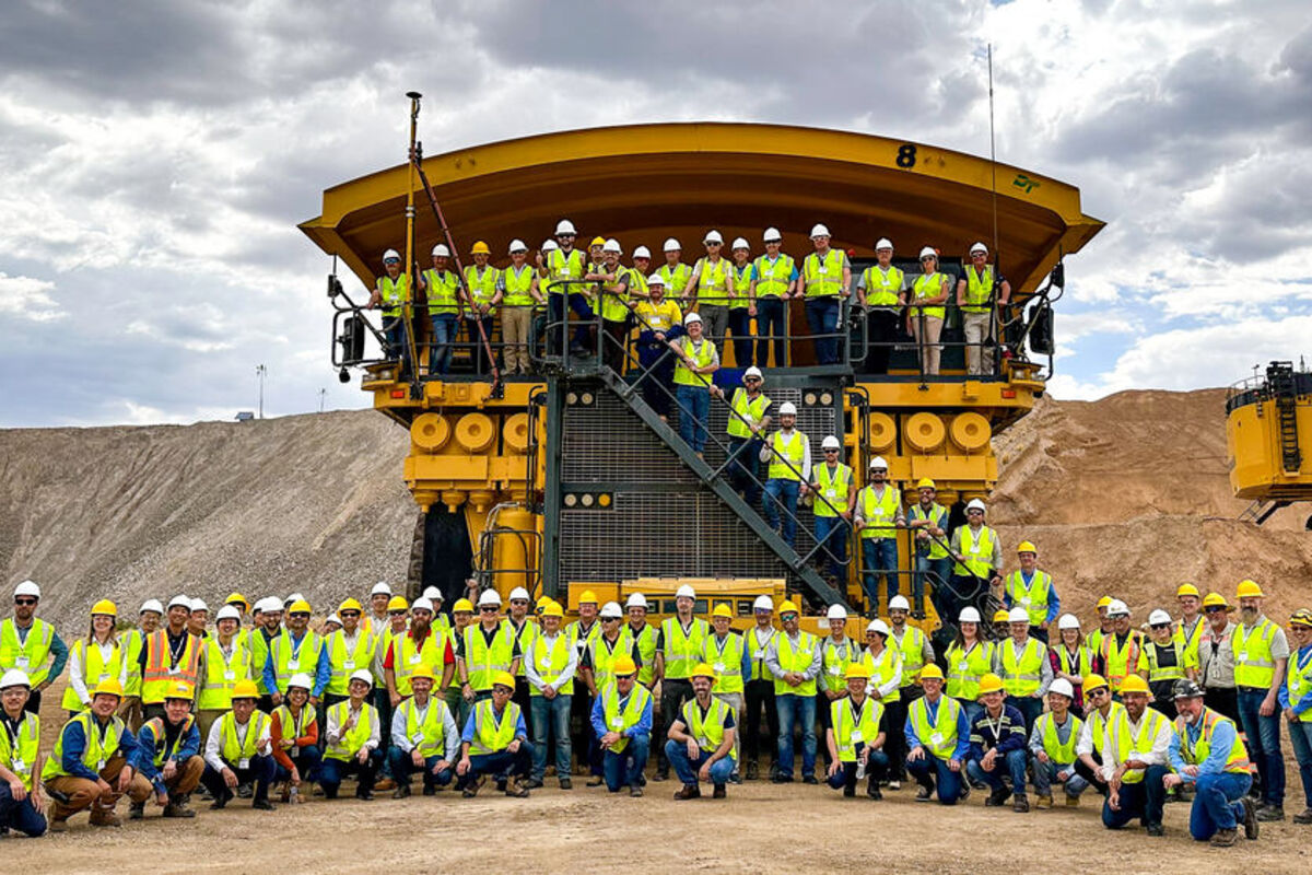 Large group in hard hats and safety vests in front of Komatsu mining truck.