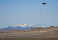 Helicopter carrying a large oval antenna over a desert region in Nevada.