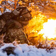 Soldier fires a machine gun while lying in the snow during winter exercises.