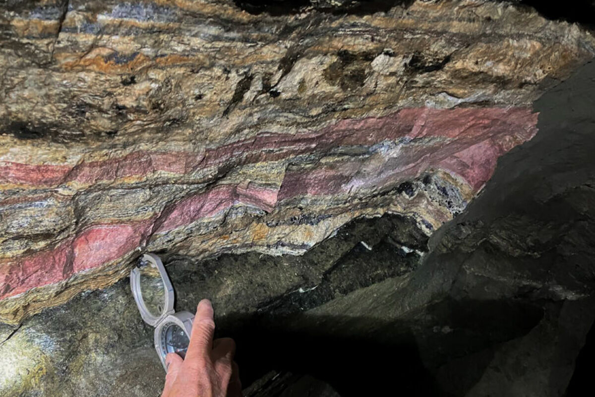 An instrument held up to pink and beige bands of underground mineralization.