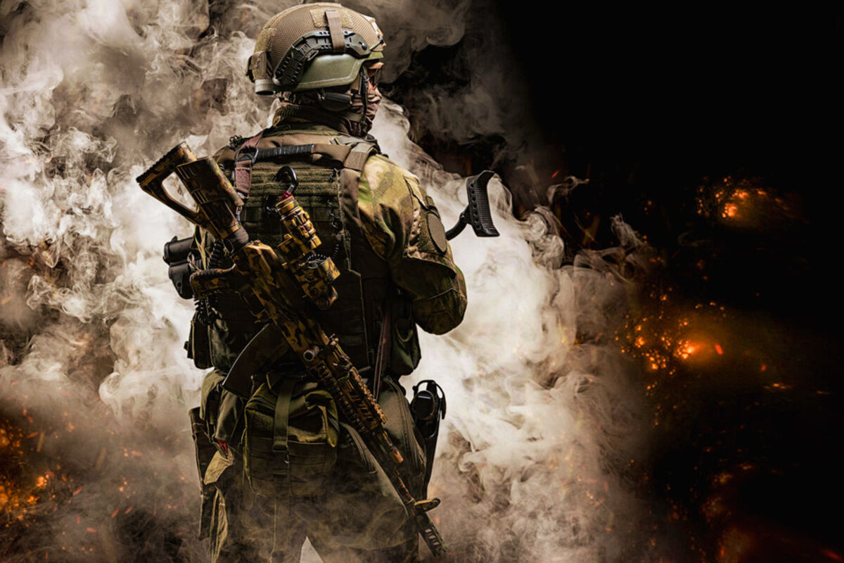 Fully equipped army soldier enters area with smoke and fire at night.