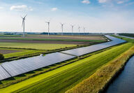 Rows of solar panels and wind turbines along the bank of a river.