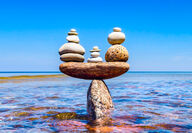 Colorful balanced stones in shallow waters near a beach.