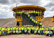 Large group in hard hats and safety vests in front of Komatsu mining truck.