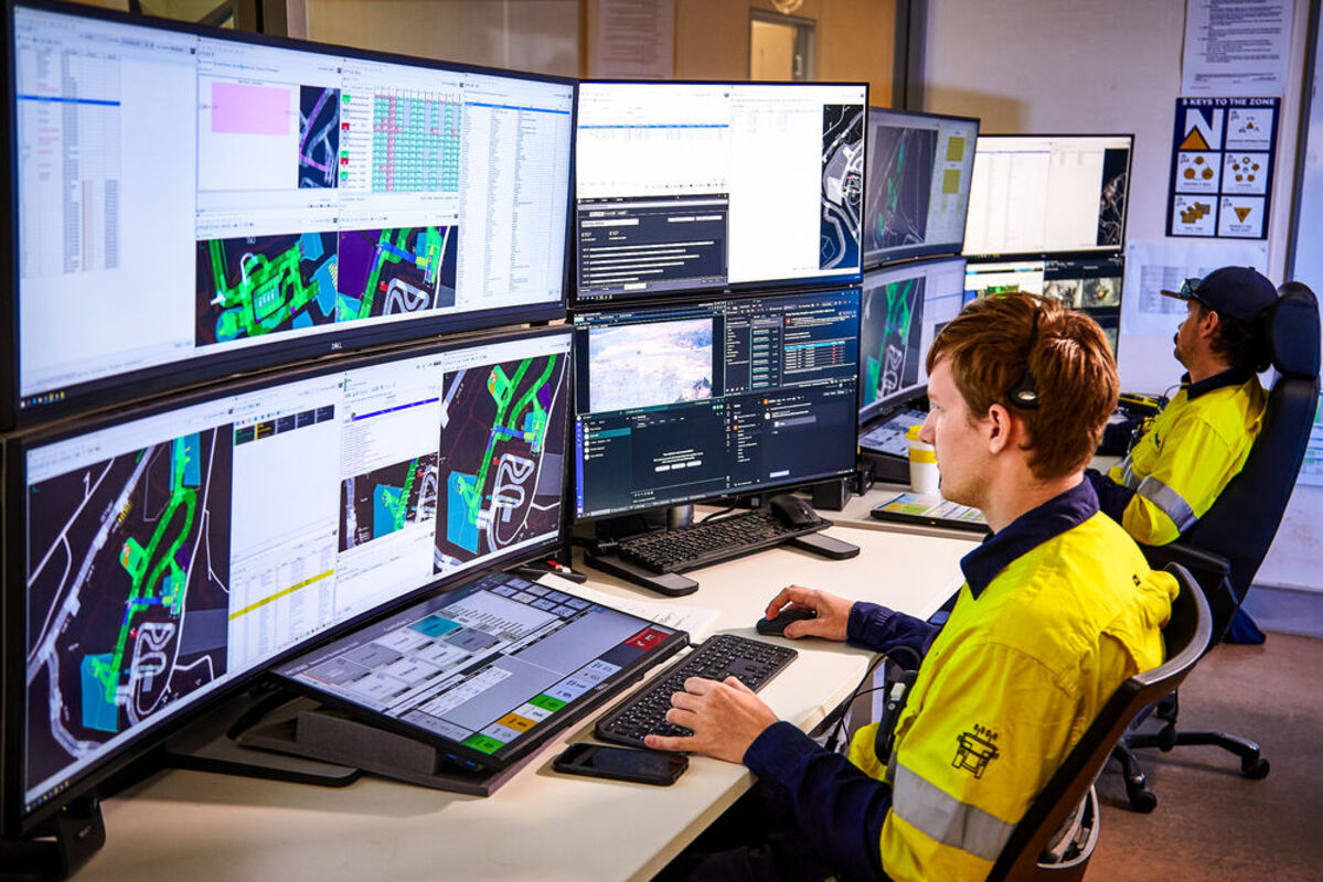 Technicians monitor autonomous mining equipment on large computer displays.