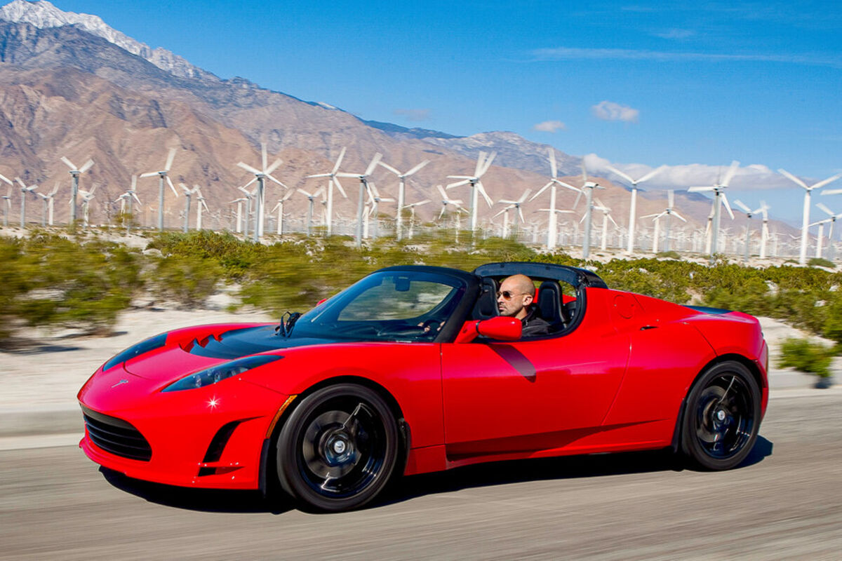Tesla%20Roadster%20cruises%20down%20highway%20in%20front%20of%20a%20large%20group%20of%20wind%20turbines%2E