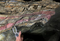 An instrument held up to pink and beige bands of underground mineralization.