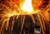 Sparks arc out of a vat being filled with molten steel.