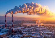 Tall industrial smoke stacks create a cloud of emissions at sunset.
