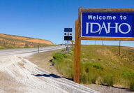 A blue “Welcome to Idaho” sign along a desert highway at the Nevada border.