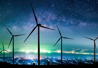 Large wind turbines silhouetted by the Milky Way and a cityscape.