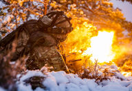 Soldier fires a machine gun while lying in the snow during winter exercises.