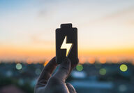 A battery cutout with a voltage symbol being held up to an orange sunset.