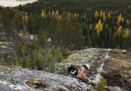 Geologist in hardhat, safety vest collecting samples from a channel cut in rock.