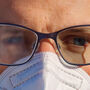 Closeup of person with mask and eyeglasses with one fogged and one clear lens.