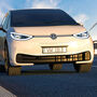 A white Volkswagen ID.4 EV travels past wind turbines on a European highway.
